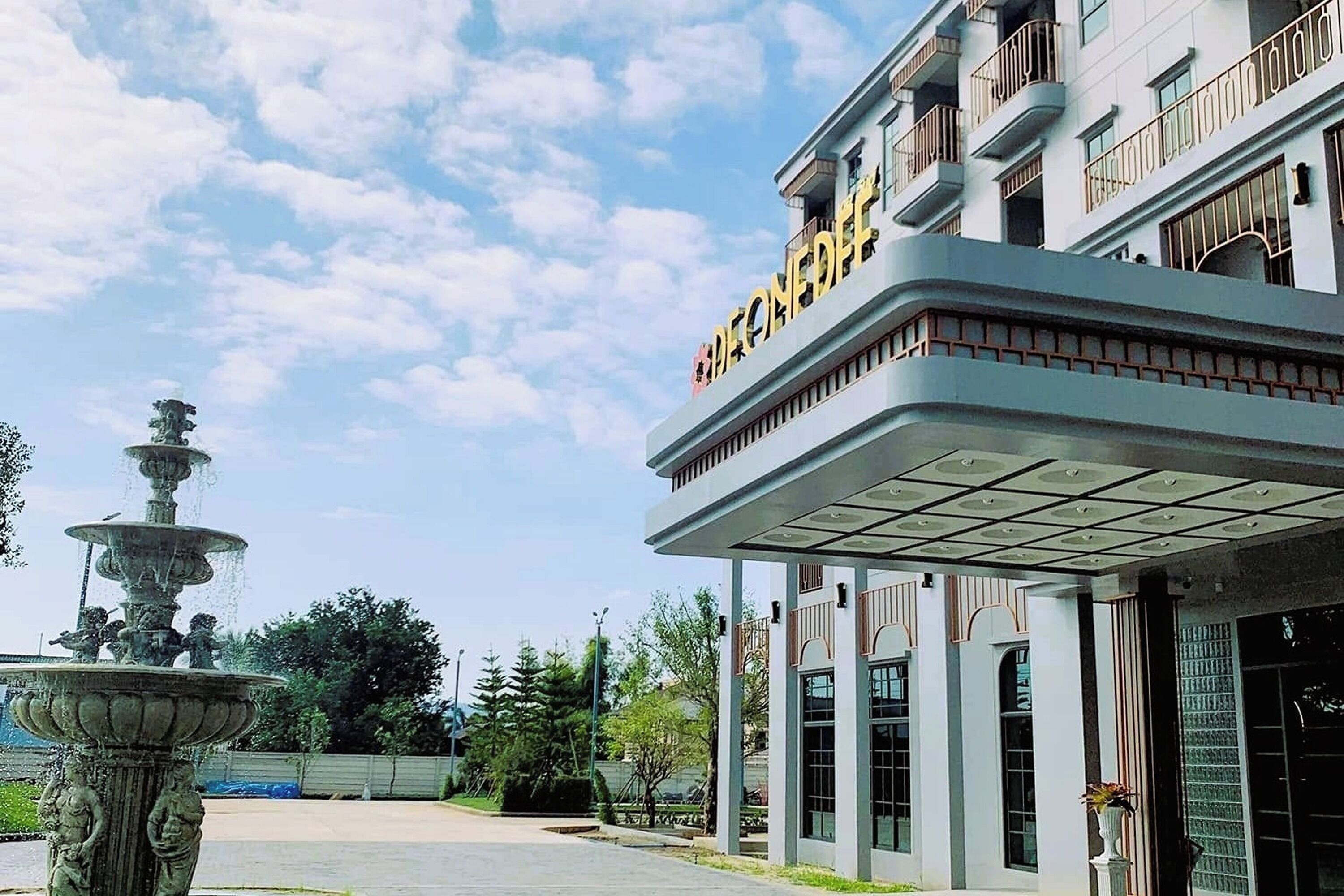 A building with a prominent entrance, a decorative fountain, and a clear sky.