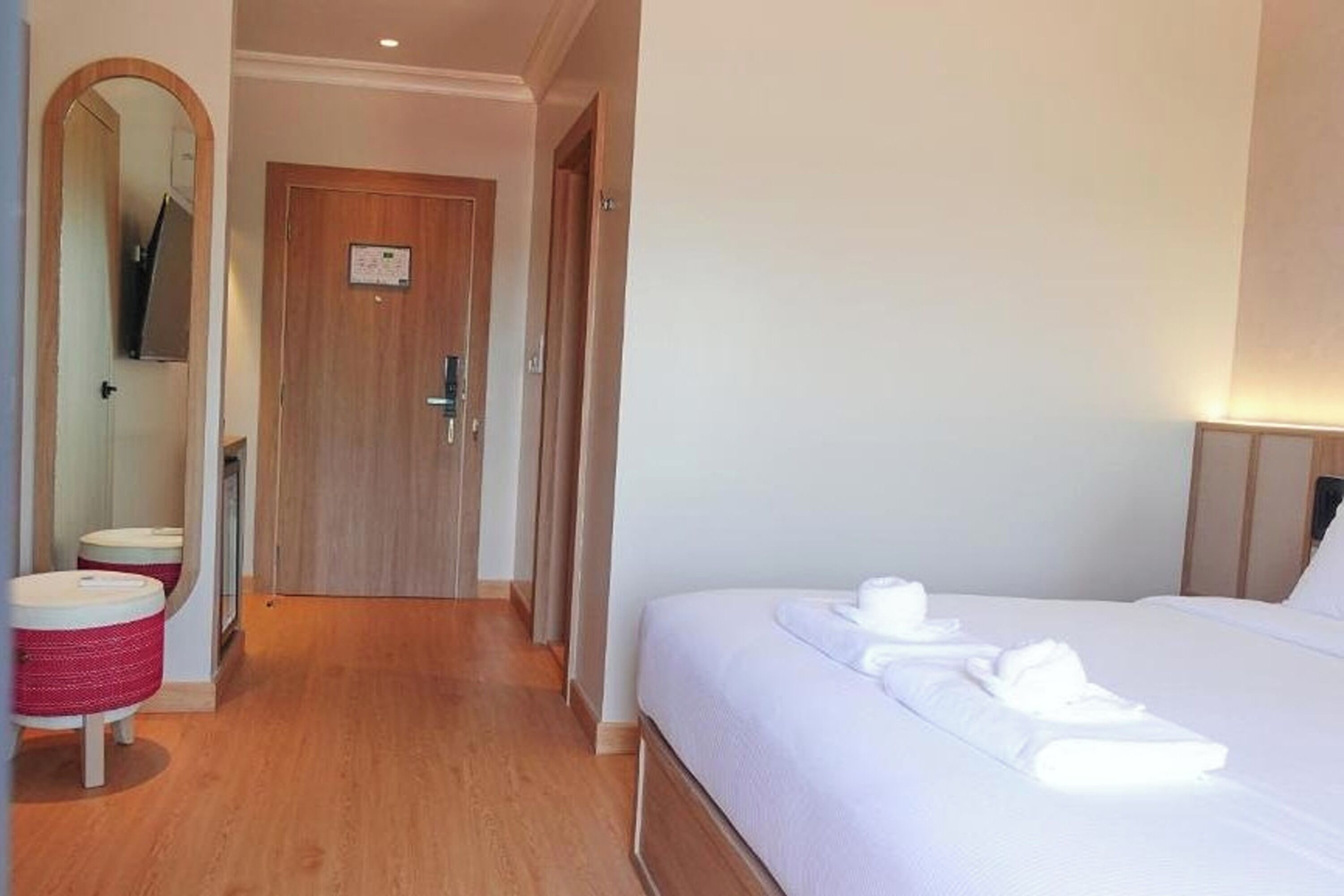 A hotel room with a wooden floor, a bed with white linens, a small round table with a red and white basket, and a wooden door with a sign.