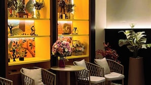 A cozy seating area with wicker chairs and a small round table, surrounded by shelves with various decorative items and plants. - Hotel De One Dee (Chiang Kham)