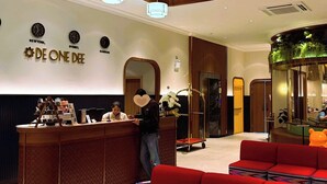 A reception area with a wooden reception desk, a red sofa, and a wall with clocks and the name "DE ONE DEE". - Hotel De One Dee (Chiang Kham)