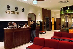 Un área de recepción con un mostrador de madera, un sofá rojo y una pared decorada con relojes y el nombre "DE ONE DEE".