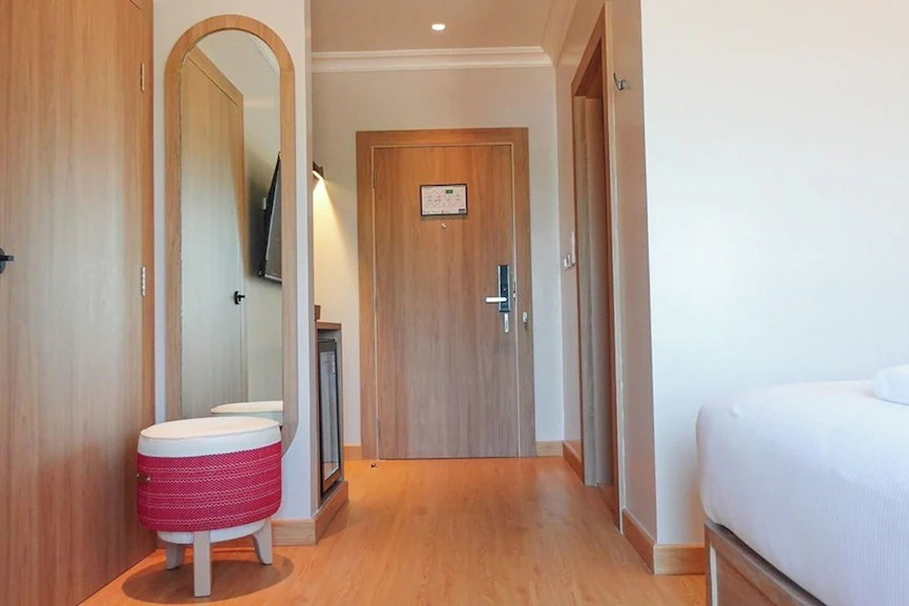 A hotel room with a wooden floor, a bed, a bathroom with a mirror, and a toilet.