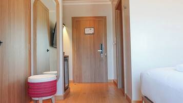 A hotel room with a wooden floor, a bed, a bathroom with a mirror, and a toilet.