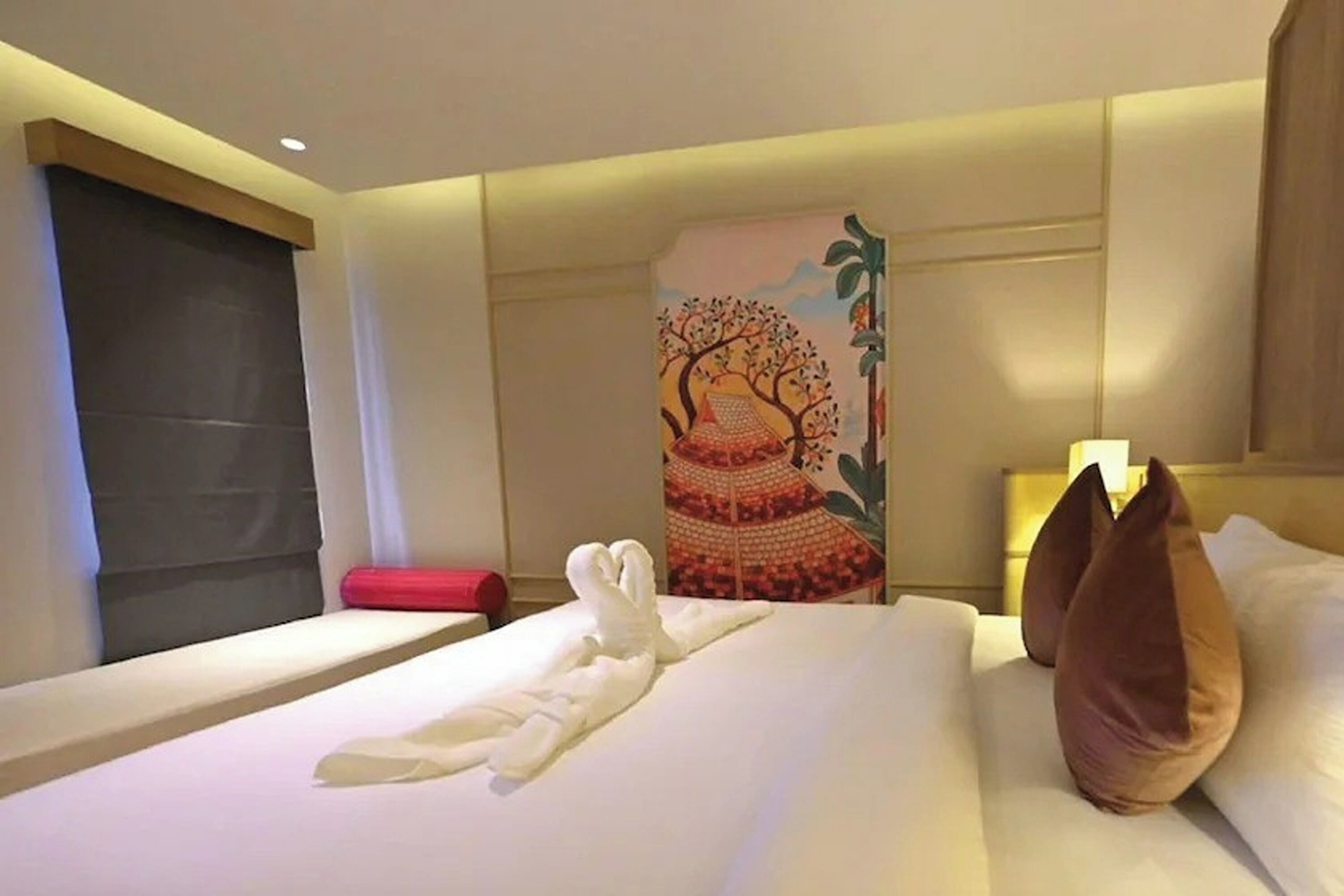 Ein Hotelzimmer mit einem ordentlich bezogenen Bett, einem roten Kissen und einer Wand mit einem farbenfrohen Wandteppich.
