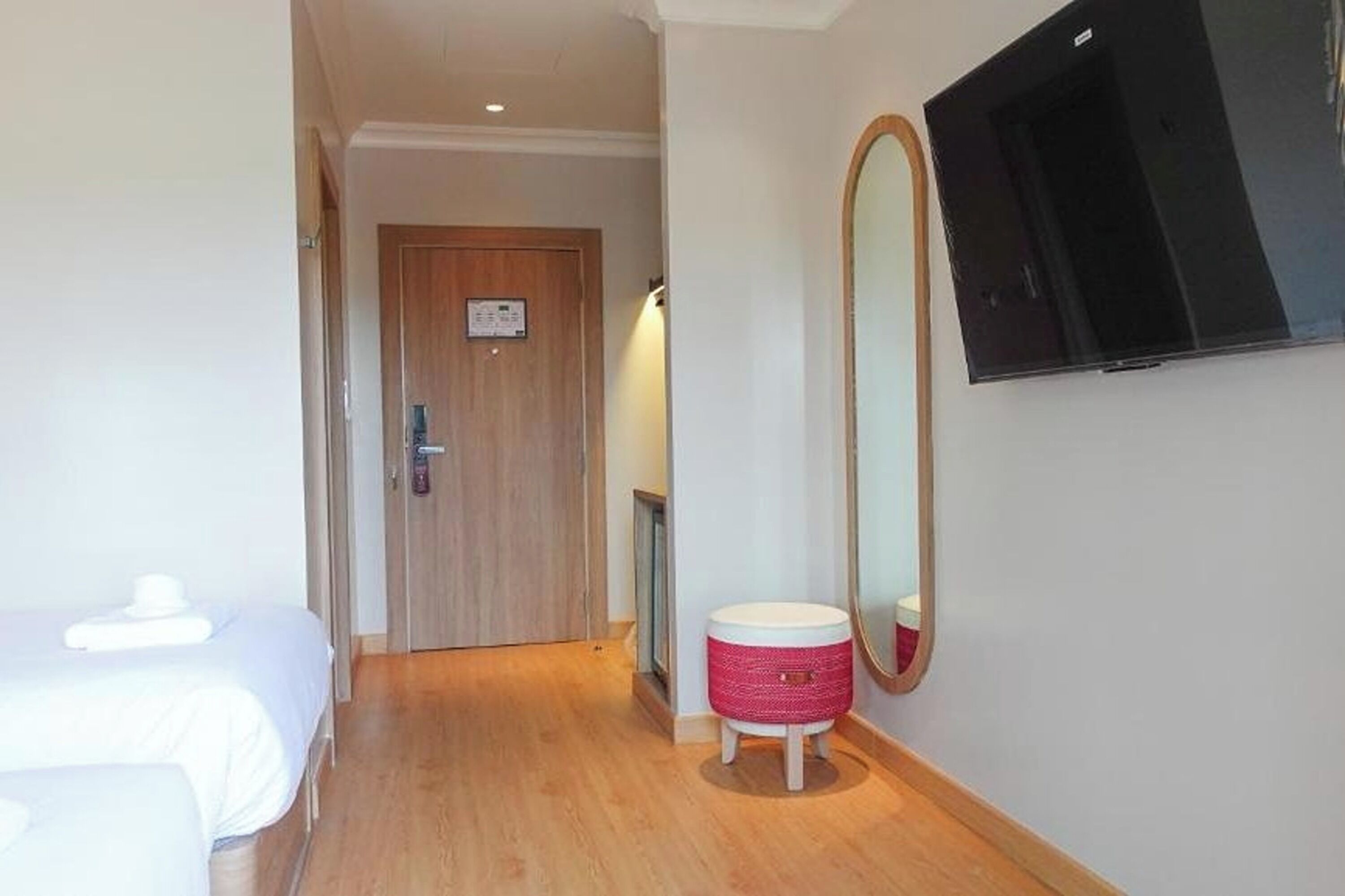 Habitación de hotel con cama, un taburete pequeño, un espejo y televisor montado en la pared.