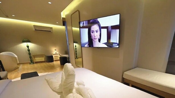 A hotel room with a bed, a TV mounted on the wall, a bedside table, and a bench. - Hotel De One Dee (Chiang Kham)