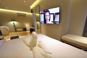 A hotel room with a bed, a TV mounted on the wall, a bedside table, and a bench. - Hotel De One Dee (Chiang Kham)