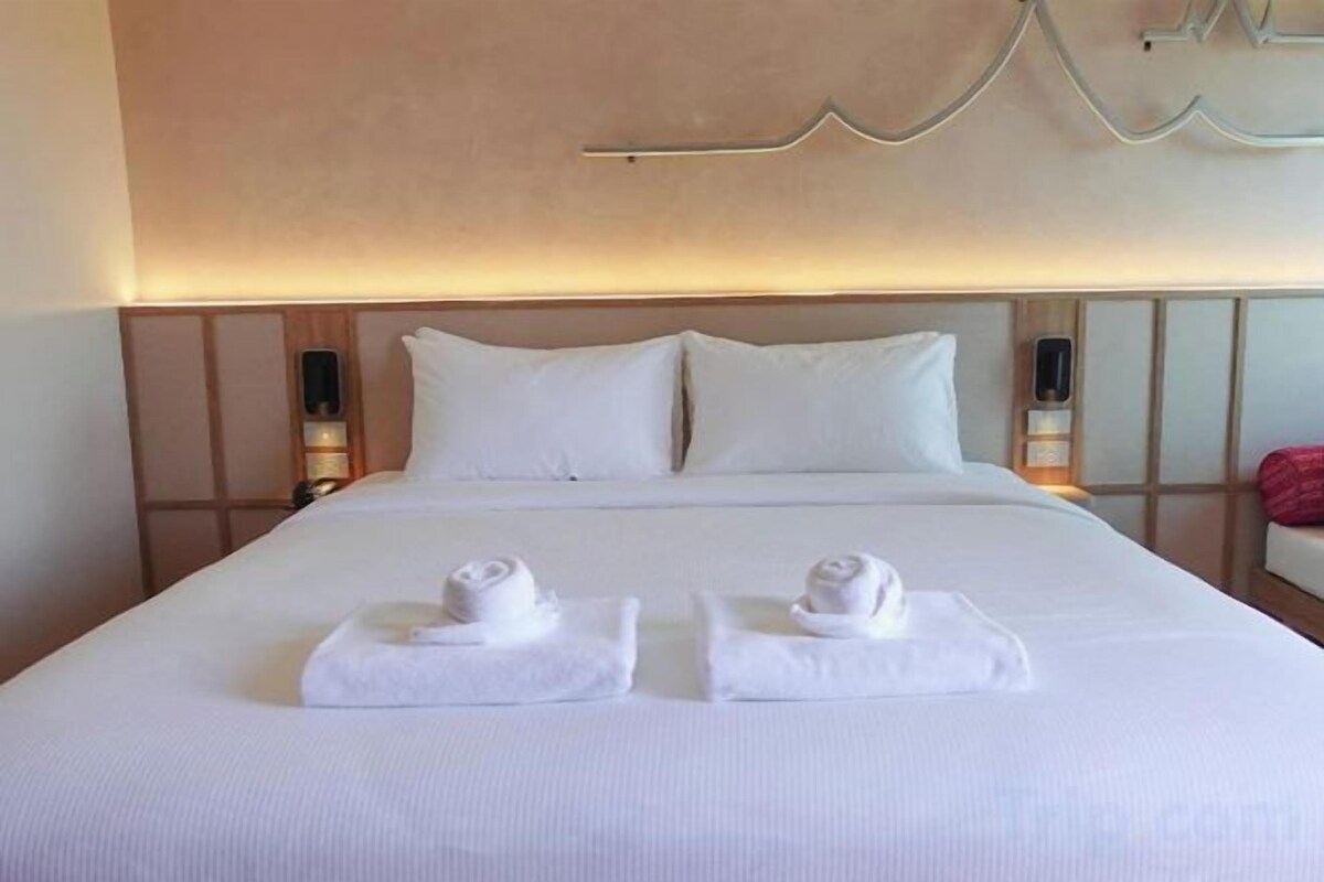 A hotel room with a neatly made bed, two pillows, bedside lamps, and a red object on the nightstand.