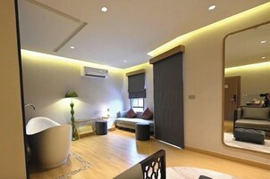 Una sala moderna con un espejo grande, un sofá, una mesa de centro y una bañera blanca distintiva.