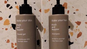 Two bottles of shower gel and shampoo with pumps, labeled 'Make your skin fresh and happier' and 'Make your hair fresh and happier' respectively, against a speckled tile background.