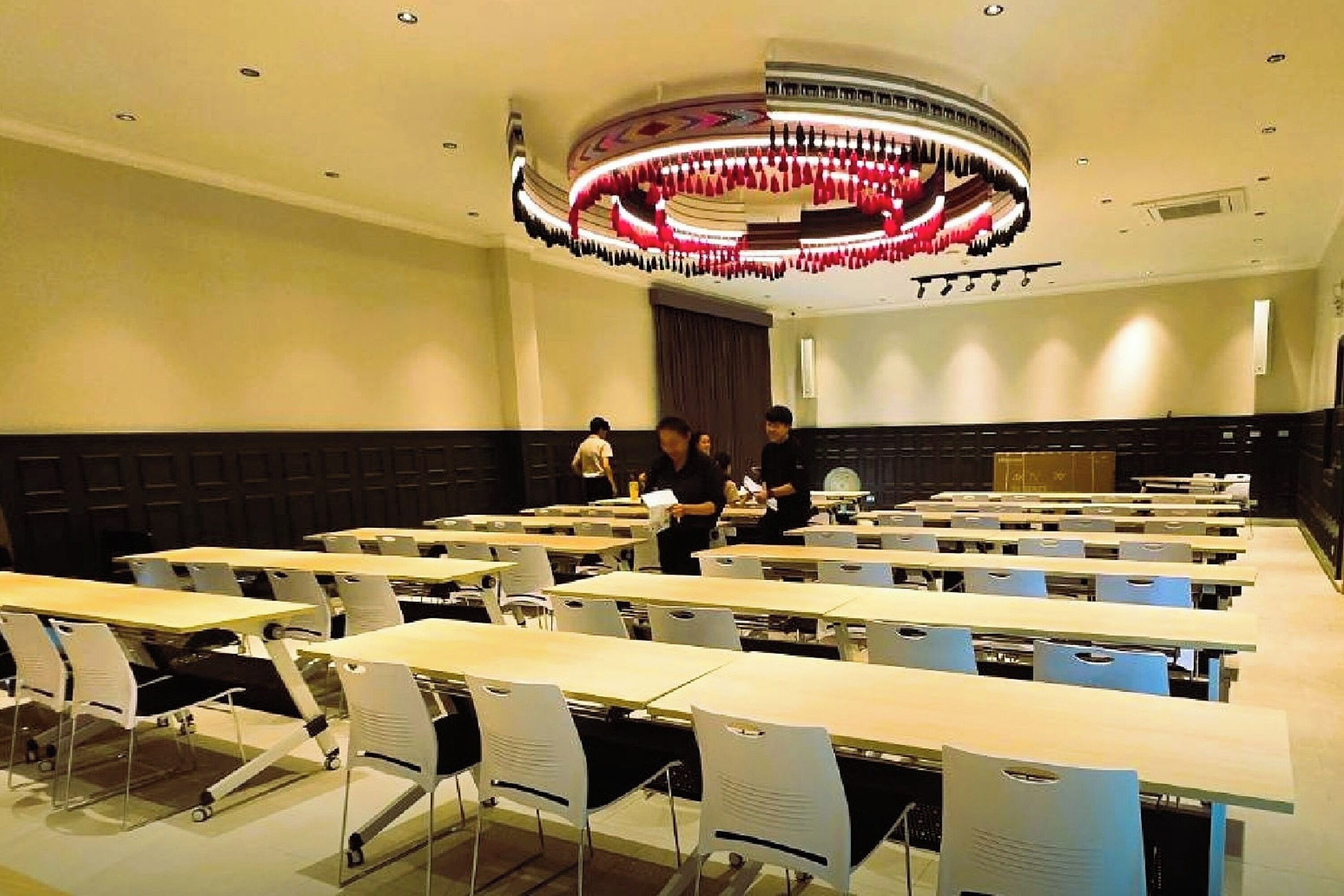 Un salón de conferencias con mesas y sillas, una gran lámpara circular y una zona de escenario.