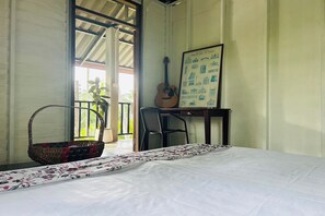 Een kamer met een bed, een gitaar, een lijst met een afbeelding van Italiaanse architectuur, een rieten mand en een stoel.