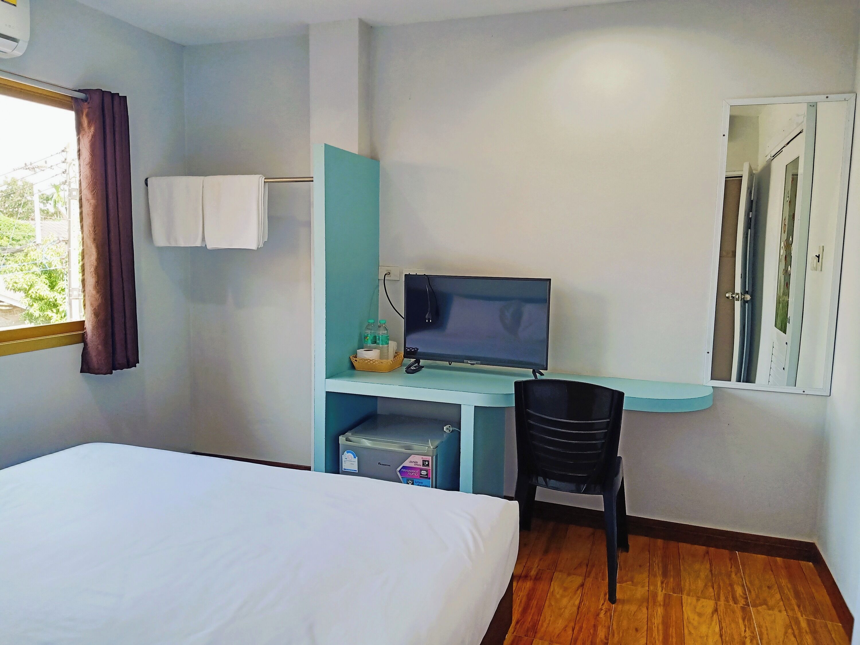 Habitación de hotel con cama, escritorio con computadora, silla, ventana con cortinas y espejo.