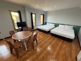 Habitación de hotel con dos camas individuales, una mesa de comedor con sillas, televisión y vistas al balcón.