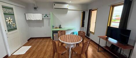 A compact living space with a dining area, kitchenette, and a TV on a stand.