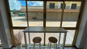 Una habitación con un ventanal grande, una mesa blanca, dos taburetes de madera y una planta en maceta.