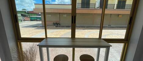 A room with a large window, a white table, two wooden stools, and a potted plant.