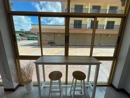 Una habitación con un ventanal grande, una mesa blanca, dos taburetes de madera y una planta en maceta.