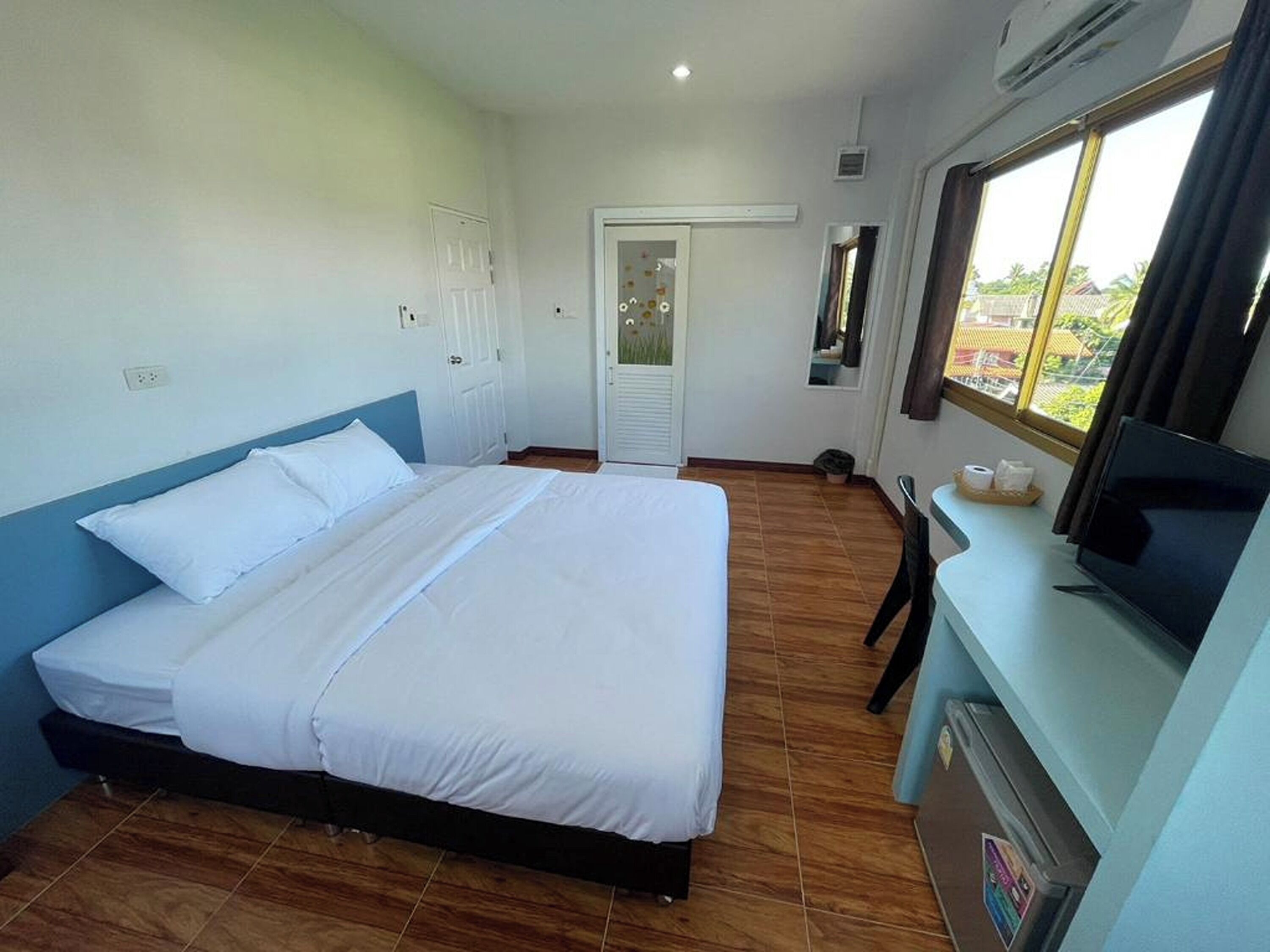 A hotel room with a bed, a TV, a window, and a door.