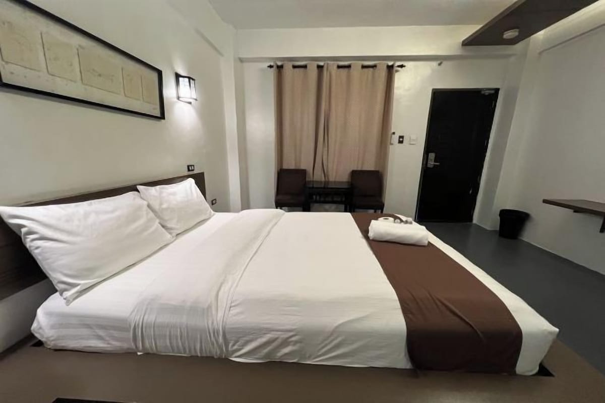 A hotel room with a large bed, a desk, a chair, and a door.