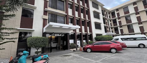 A modern building with a parking area, a red car, and two scooters.