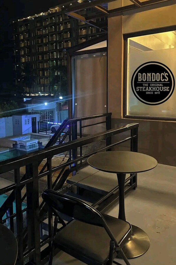 Un restaurante con mesas al aire libre, un letrero que dice 'Bondoc's Steakhouse' y una vista de un edificio al fondo.
