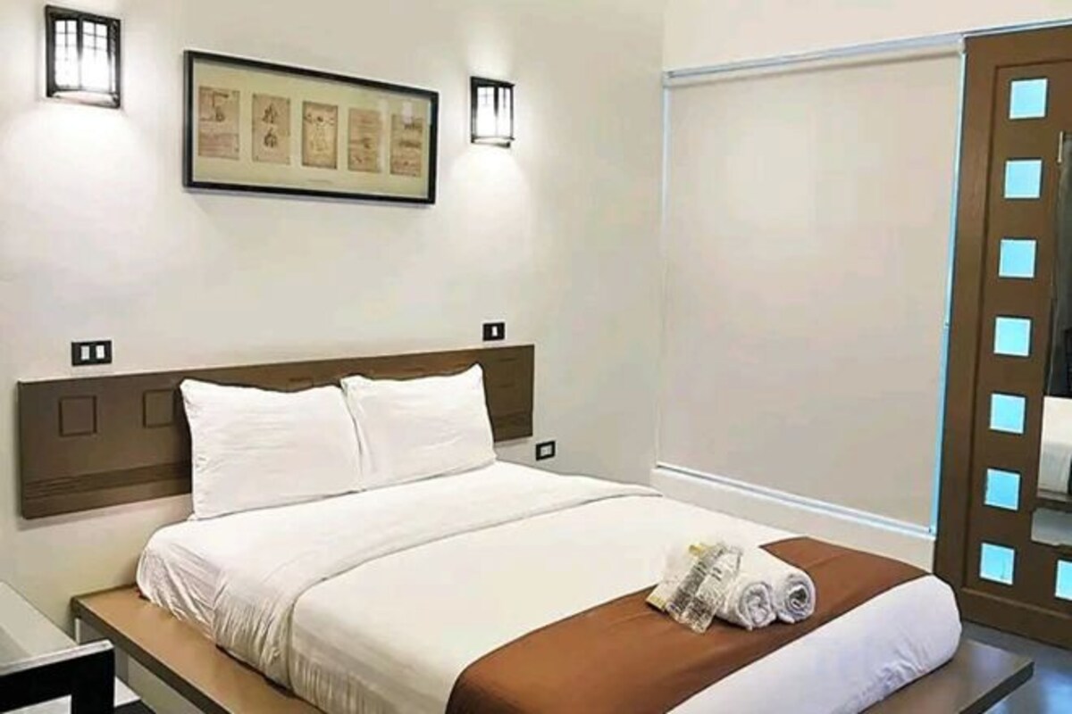 A hotel room with a bed, a nightstand, a framed picture on the wall, and two wall-mounted lights.