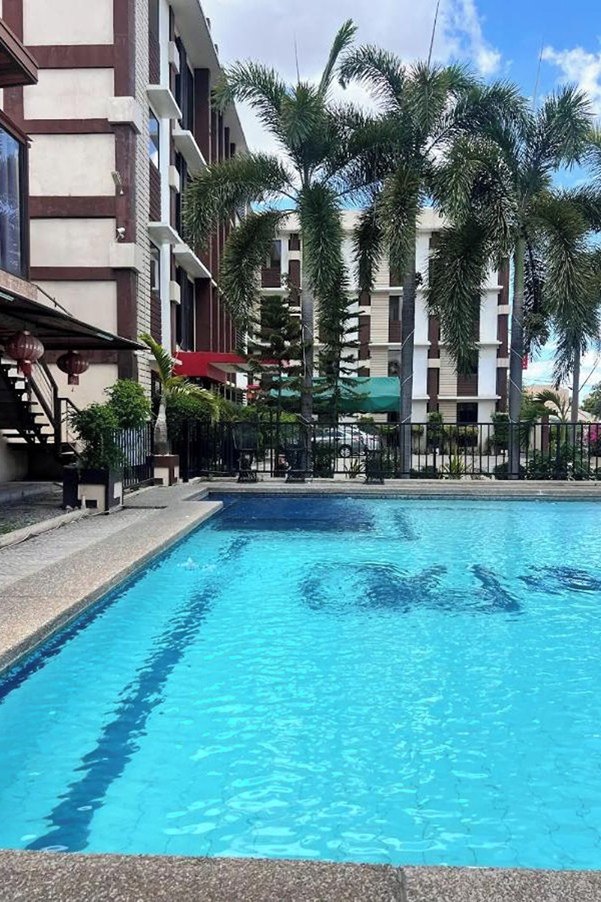A swimming pool surrounded by palm trees and a multi-story building with balconies.