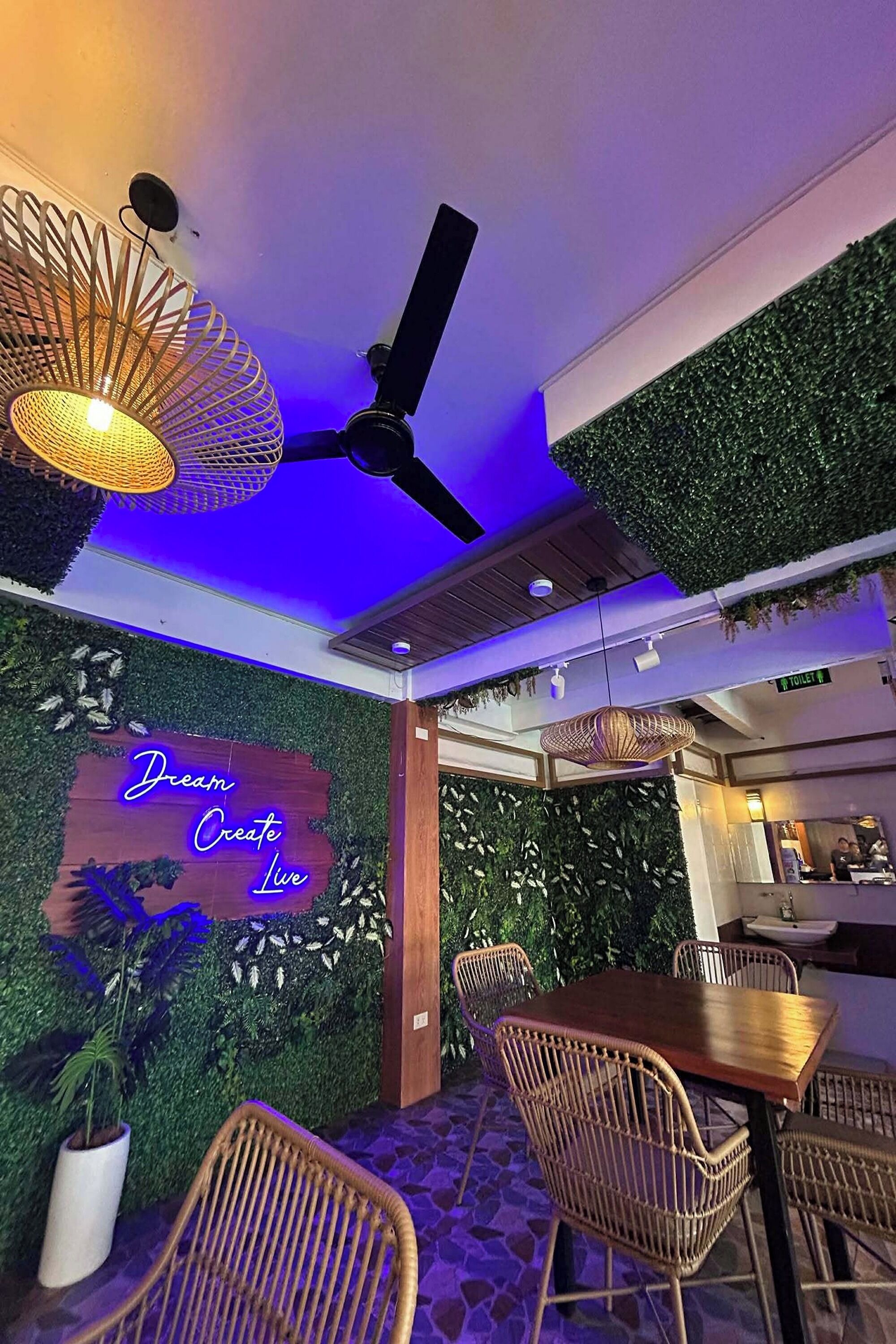 A restaurant interior with a ceiling fan, hanging lights, a neon sign, and a wall with greenery.