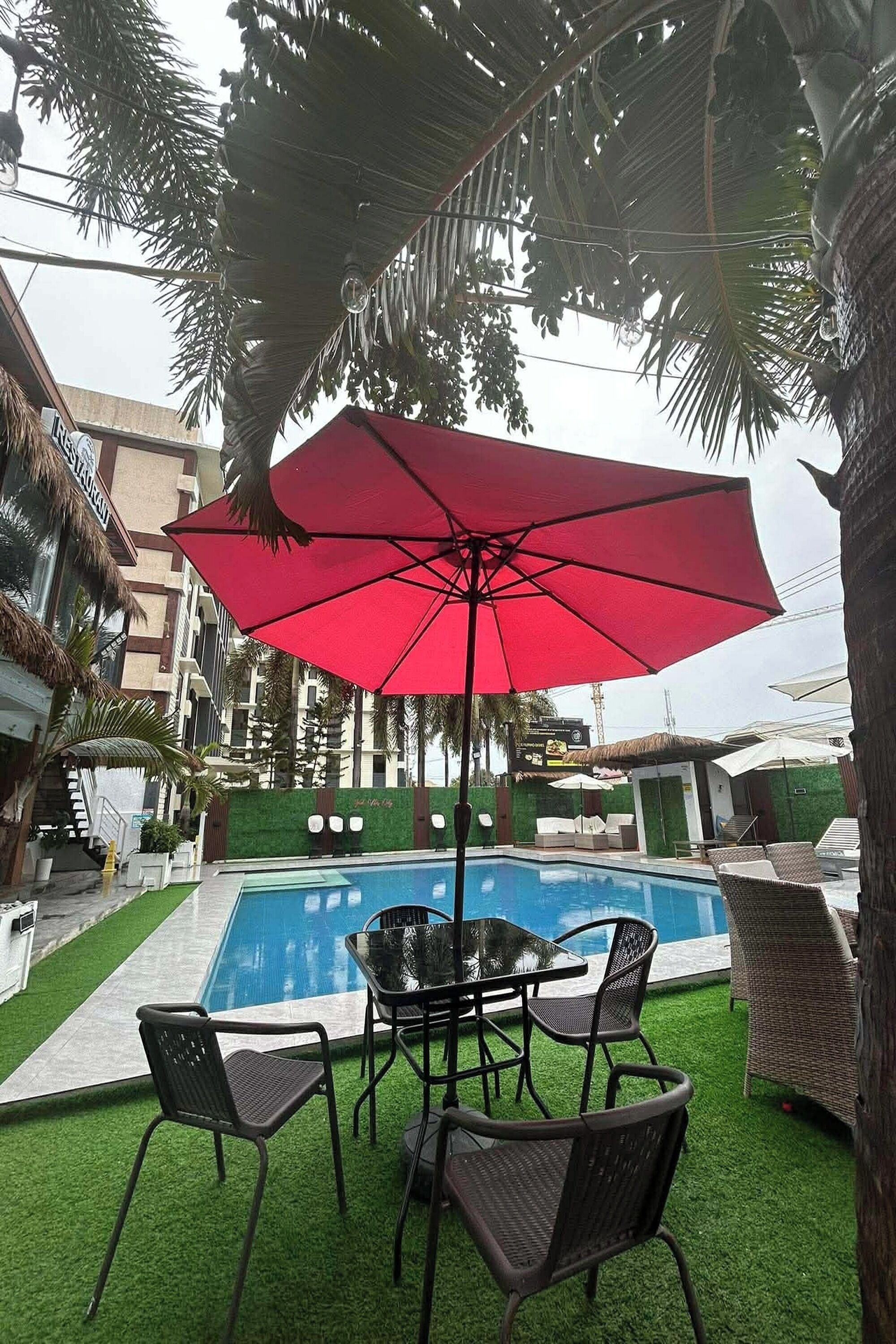 A swimming pool with a red umbrella, surrounded by artificial grass and wicker furniture.