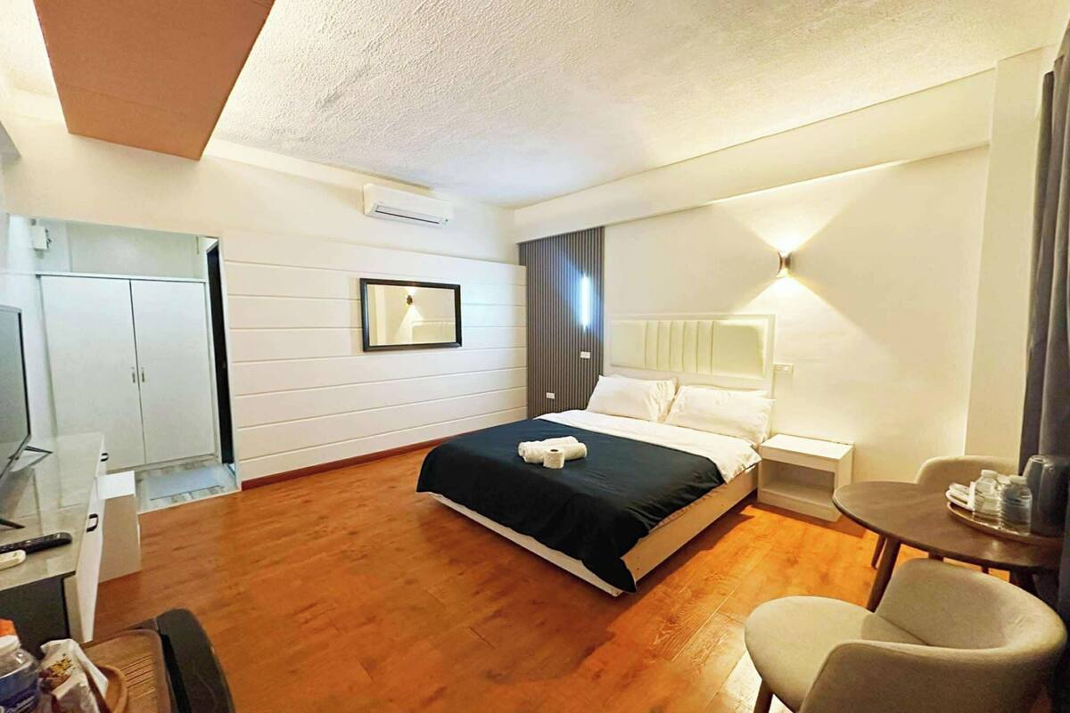 Quarto de hotel com cama, escrivaninha, cadeira, espelho e mesa de cabeceira.