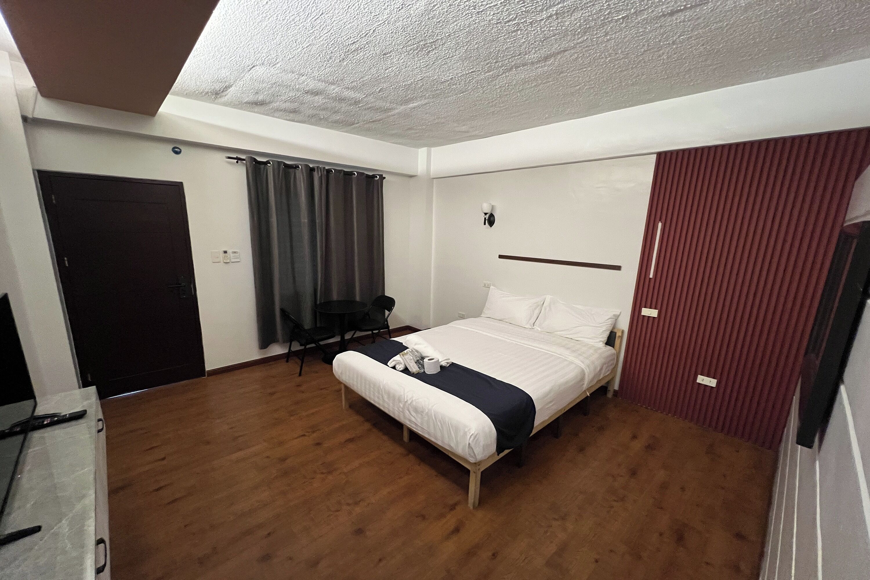 A bedroom with a bed, a desk, a chair, a door, and a curtain.
