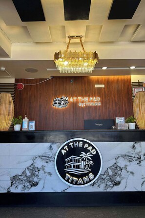 Un comptoir d'accueil d'hôtel agrémenté d'un lustre, de boiseries et d'un mur en marbre orné du logo de l'hôtel.