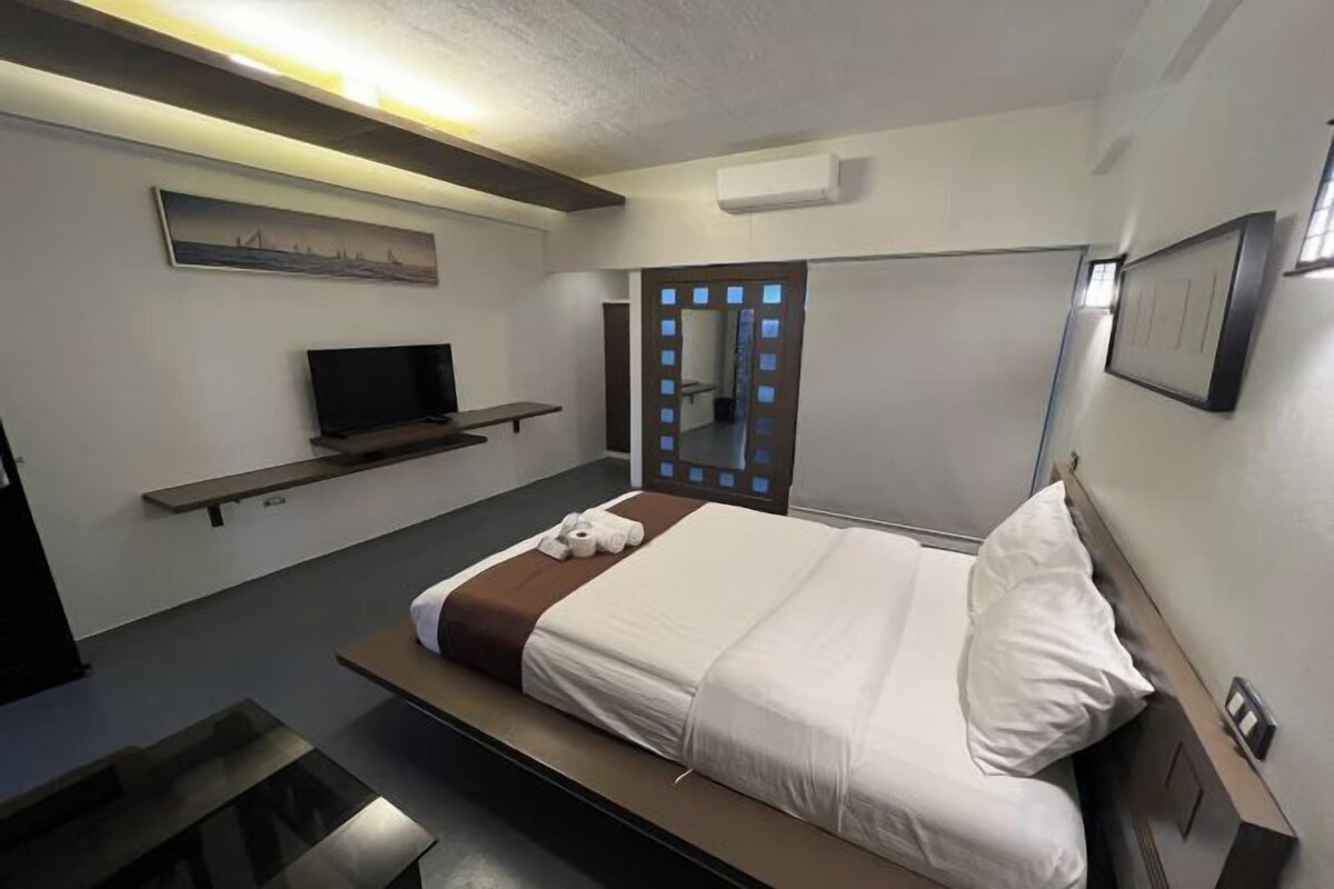 A modern hotel room with a bed, a flat-screen TV, a bedside table, and a large window.