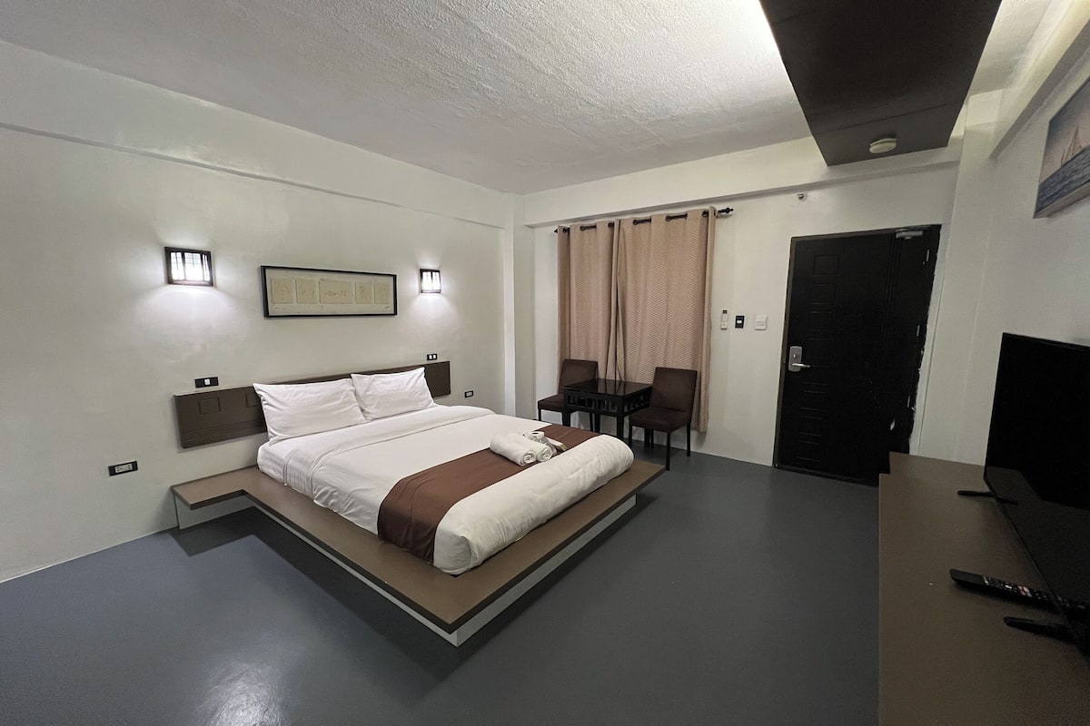 Quarto de hotel moderno com uma cama grande, mesas de cabeceira, uma escrivaninha e uma TV.