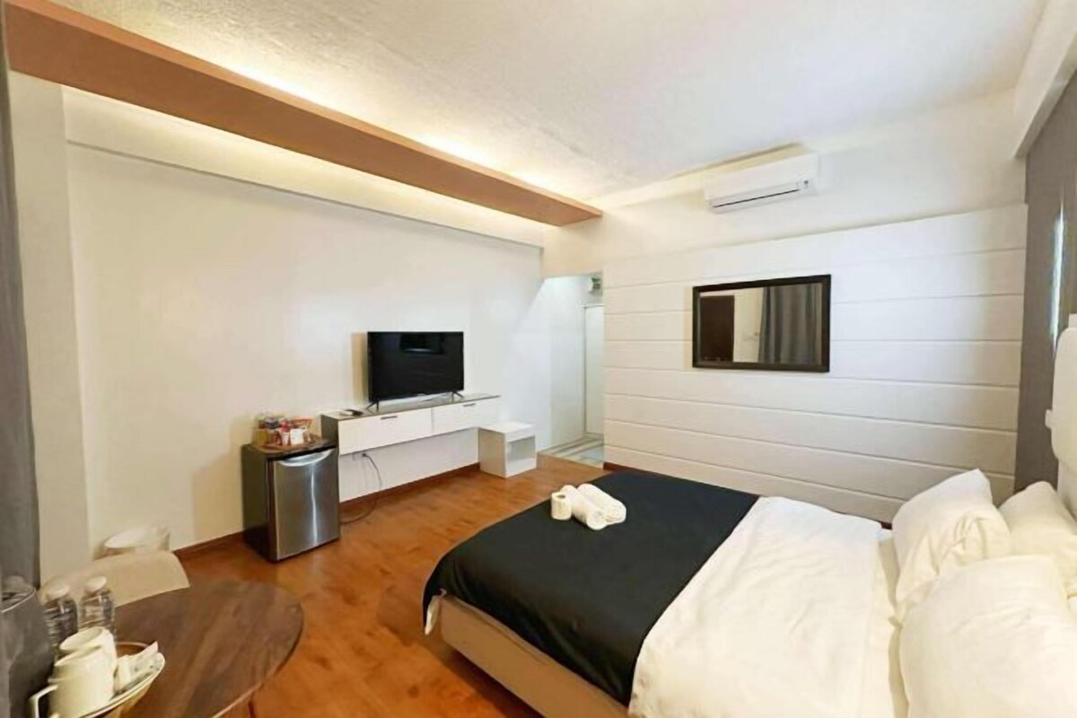 Habitación de hotel con cama, televisor, escritorio pequeño y espejo.