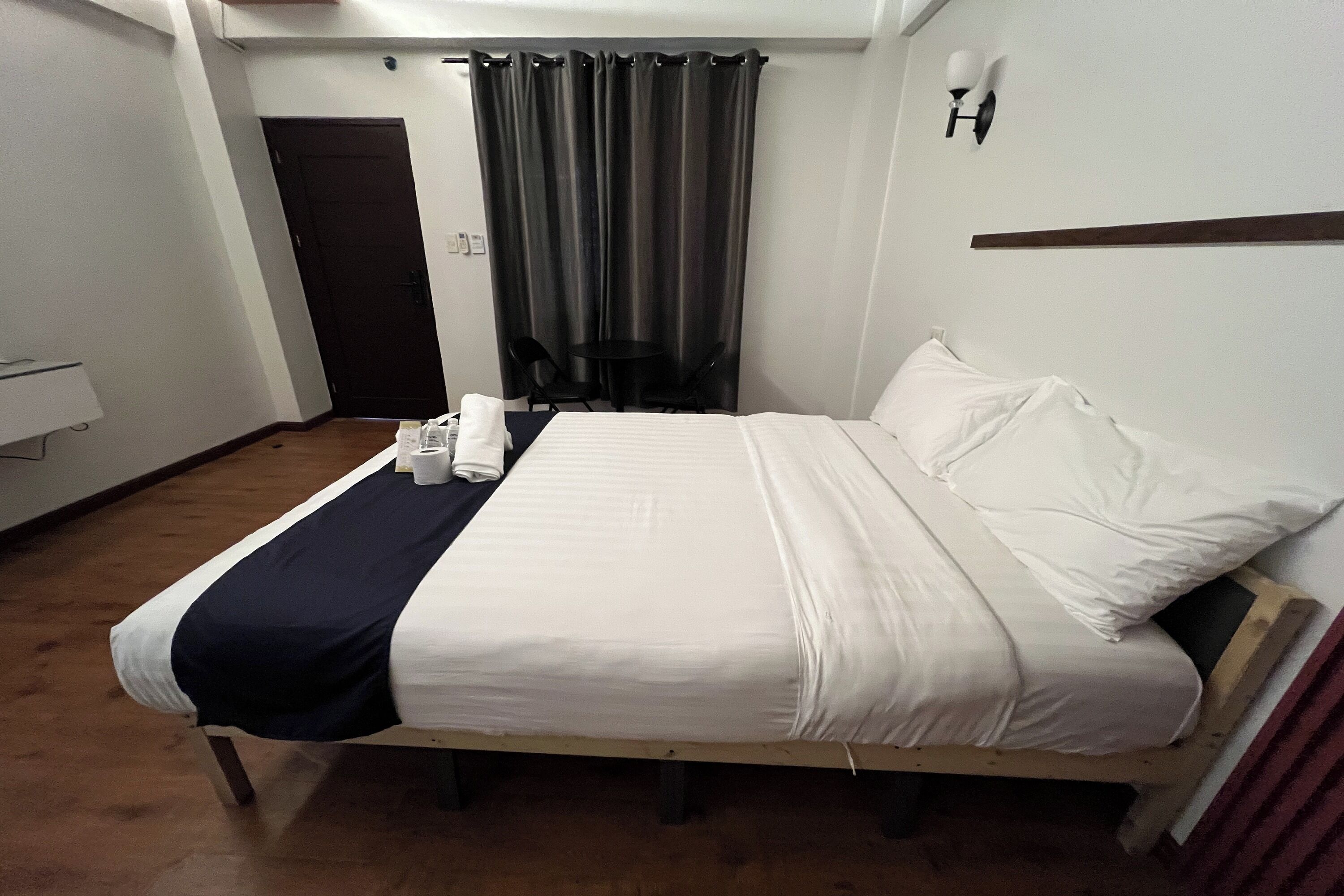 Ein Hotelzimmer mit einem Bett, einem Schreibtisch, einem Stuhl, einem Vorhang und einer Wandleuchte.