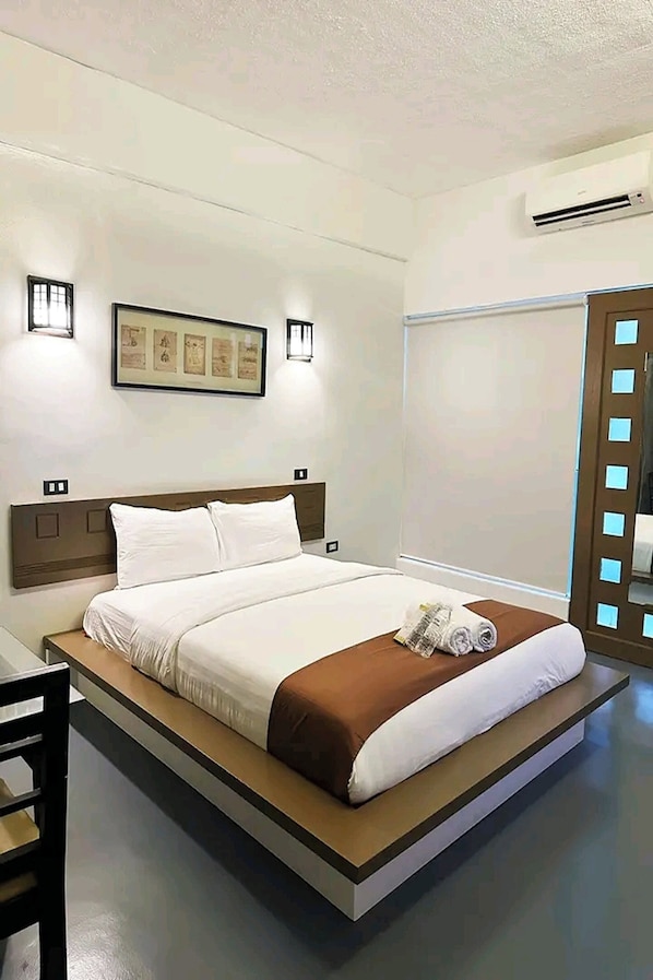A modern hotel room with a large bed, a wooden headboard, wall-mounted lights, a framed picture, and a large mirror. - At The Pad Hotel and Resort near Clark Airport (Angeles City)