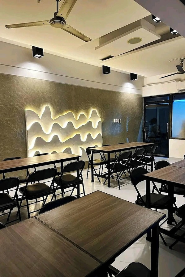 A modern dining area with wooden tables and black chairs, a ceiling fan, recessed lighting, and a textured wall feature.