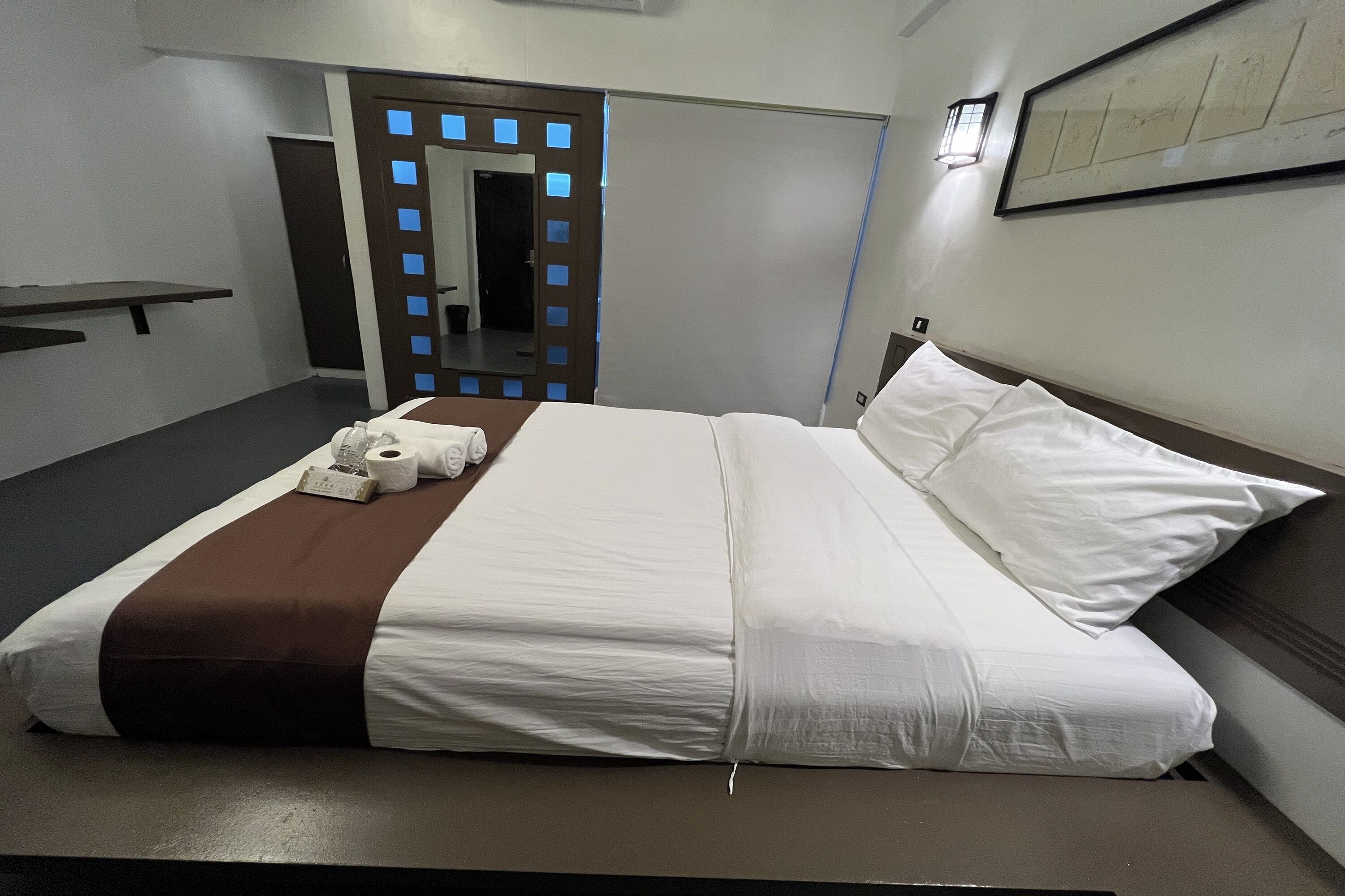 A neatly made bed with white and brown bedding, a bedside table with a lamp, and a framed picture on the wall.