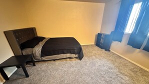 Un dormitorio con cama, mesita de noche, ventana con cortinas y suelo alfombrado.