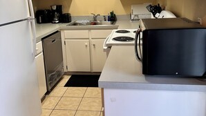 Una cocina compacta con armarios blancos, un refrigerador de acero inoxidable, un lavavajillas, una estufa y un microondas.