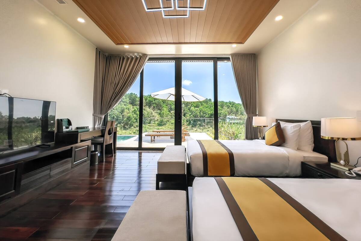 A modern hotel room with a large bed, a television, and a balcony with a view of greenery.