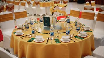 A round table set for a formal event with white chairs and gold sashes, a vase with yellow flowers, and a menu sign.