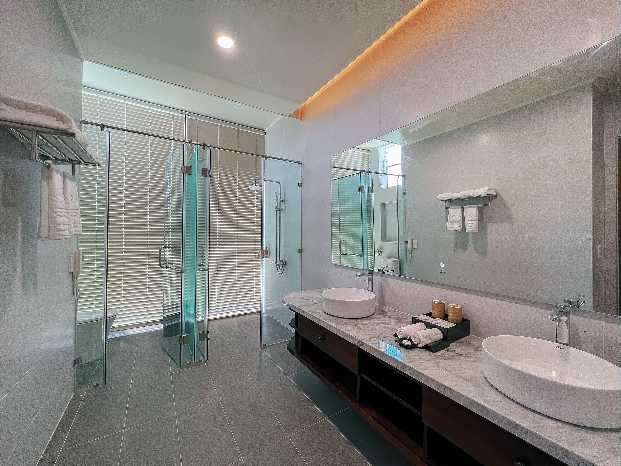 A modern bathroom with a glass shower enclosure, two sinks, a large mirror, and a towel rack.