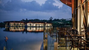 En restaurang vid vattnet med uteservering och utsikt över en lugn vattenyta. Restaurangen har en modern arkitektonisk design med stora fönster och en distinkt takkonstruktion.