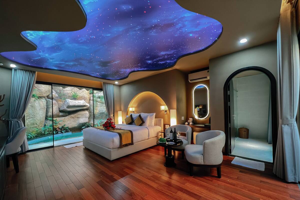 A modern hotel room with a starry ceiling, a bed, a seating area, and a view of a rocky outdoor area.