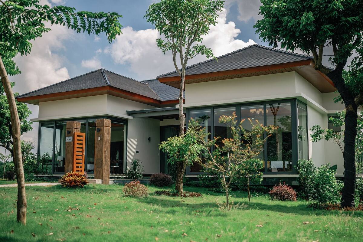 A modern two-story house with a large glass facade, a wooden staircase, and a well-maintained garden.