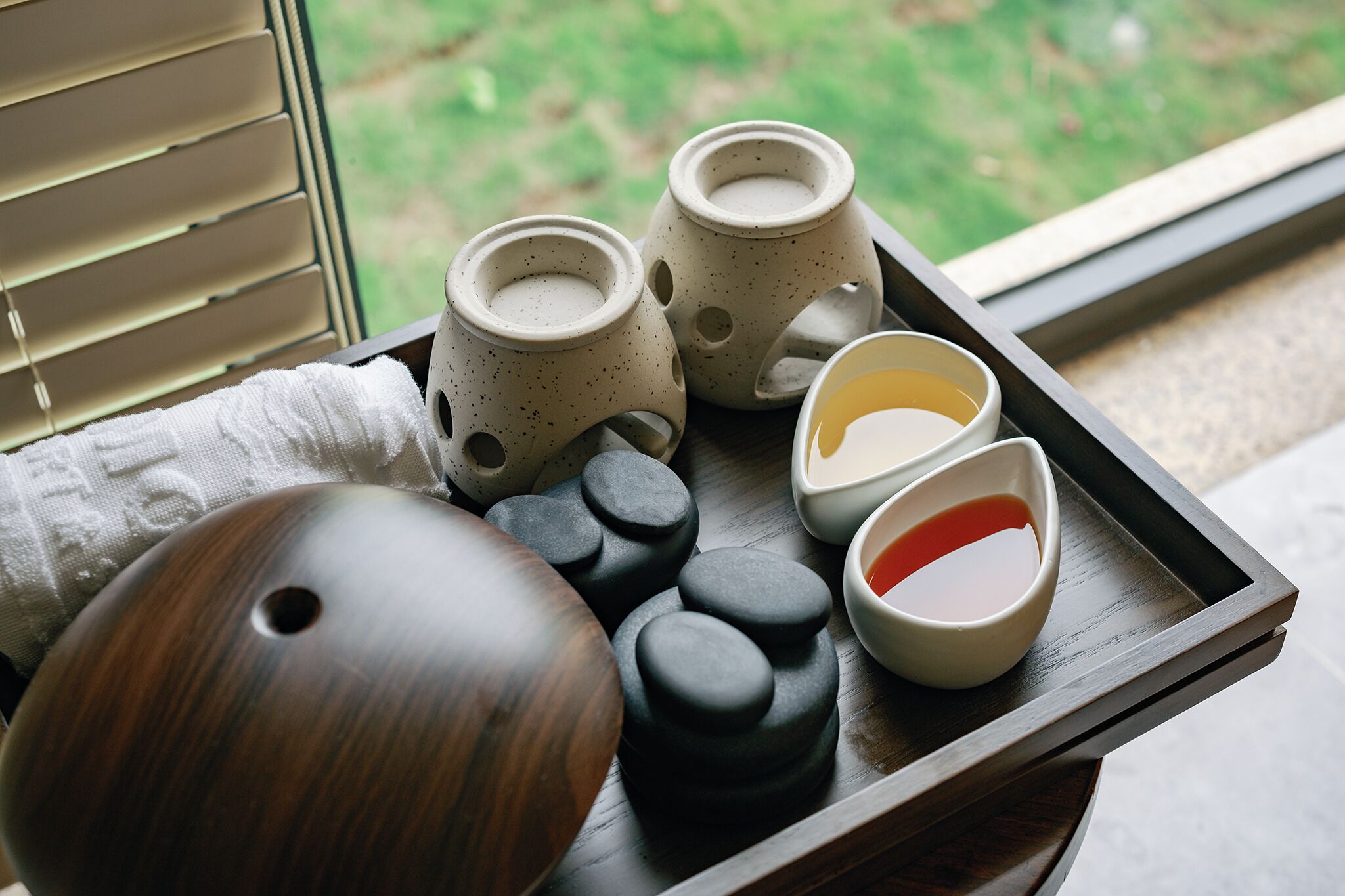 A tray with various items including a wooden object, black and beige ceramic cups, and a bowl with a red interior.