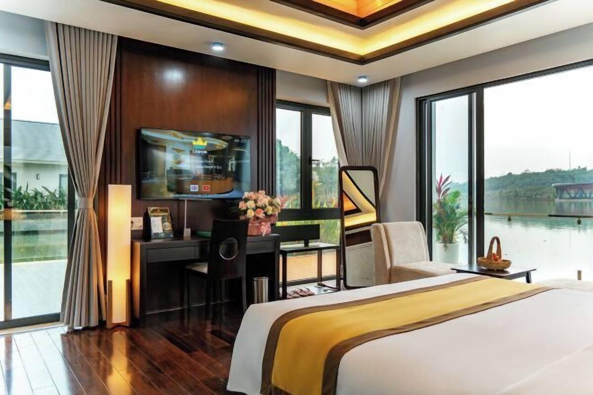 A modern hotel room with a large bed, a desk with a TV, and a view of a body of water.